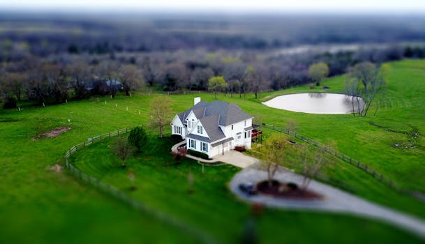 Aerial shot of a charming rural home surrounded by lush green fields and a tranquil pond.